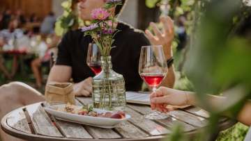 Pärchen sitzt an einem Holztisch mit sommerlicher Dekoration sowie Snacks und einem Glas Wein