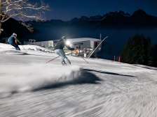 Zwei Skifahrer blicken beim Nachtskifahren am Pizol über das beleuchtete Rheintal
