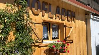 Eine Holzhütte mit Blumen und der Aufschrift "Hofladen"