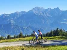 Zwei Personen fahren mit Alpine Scootern talwärts und im Hintergrund sind die Berge der Bündner Herrschaft zu sehen