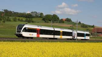 Zug mit 3 Wagons fährt durch frühlingshafte Landschaft in der Schweiz