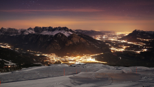 Ausblick aufs winterliche Sarganserland bei Nacht. Im Vordergrund ist eine Skipiste zu sehen. Im Tal sieht man die bunten Lichter.