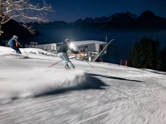 Zwei Skifahrer blicken beim Nachtskifahren am Pizol über das beleuchtete Rheintal